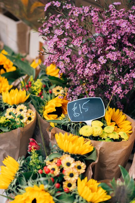 An assortment of fresh flower bouquets arranged at a market stall, featuring vibrant yellow sunflowers, delicate cream and pink daisy-like flowers, and small red and yellow blooms, all wrapped in brow