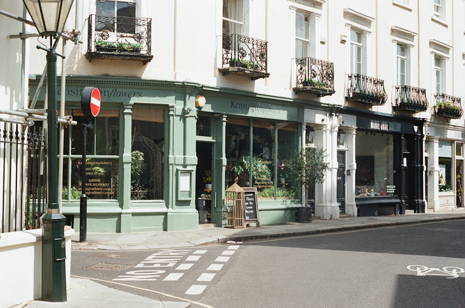 The image depicts a charming florist shop on Edgware High Street, with a pastel green facade and large display windows showcasing fresh floral arrangements. Above the shop, several small wrought-iron